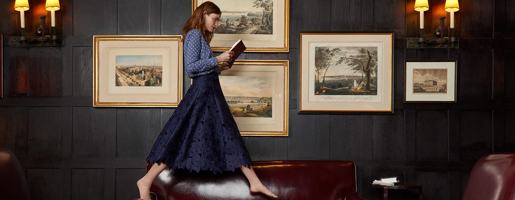 Woman walking on a couch reading a book 